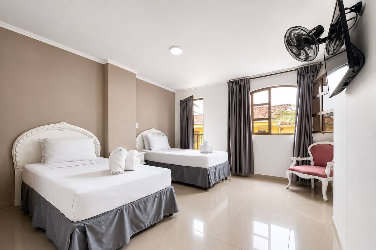 Una habitación de hotel con dos camas, televisión, una silla y ventana con cortinas.