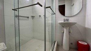 A bathroom with a glass-enclosed shower, a white sink, and a red trash bin.