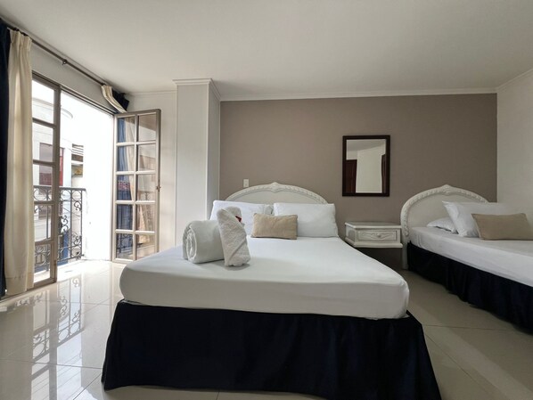 A hotel room with two beds, a large window, a balcony, and a mirror on the wall. - Hotel Suite Santa Rosa (Santa Rosa de Cabal)