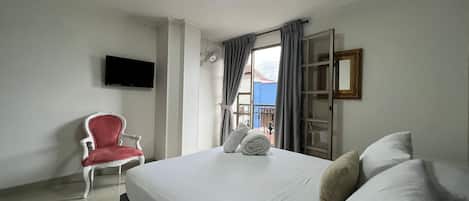 A hotel room with a bed, a chair, a TV, and a window with curtains.