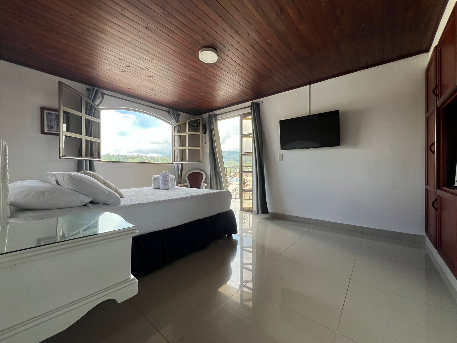 Un dormitorio con cama, televisor, ventana con vistas y techo de madera.