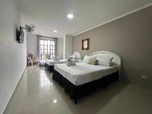 A hotel room with a large bed, two smaller beds, a TV, a fan, and a window with curtains. - Hotel Suite Santa Rosa (Santa Rosa de Cabal)
