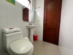 A bathroom with a toilet, sink, mirror, and a wooden door. - Hotel Suite Santa Rosa (Santa Rosa de Cabal)