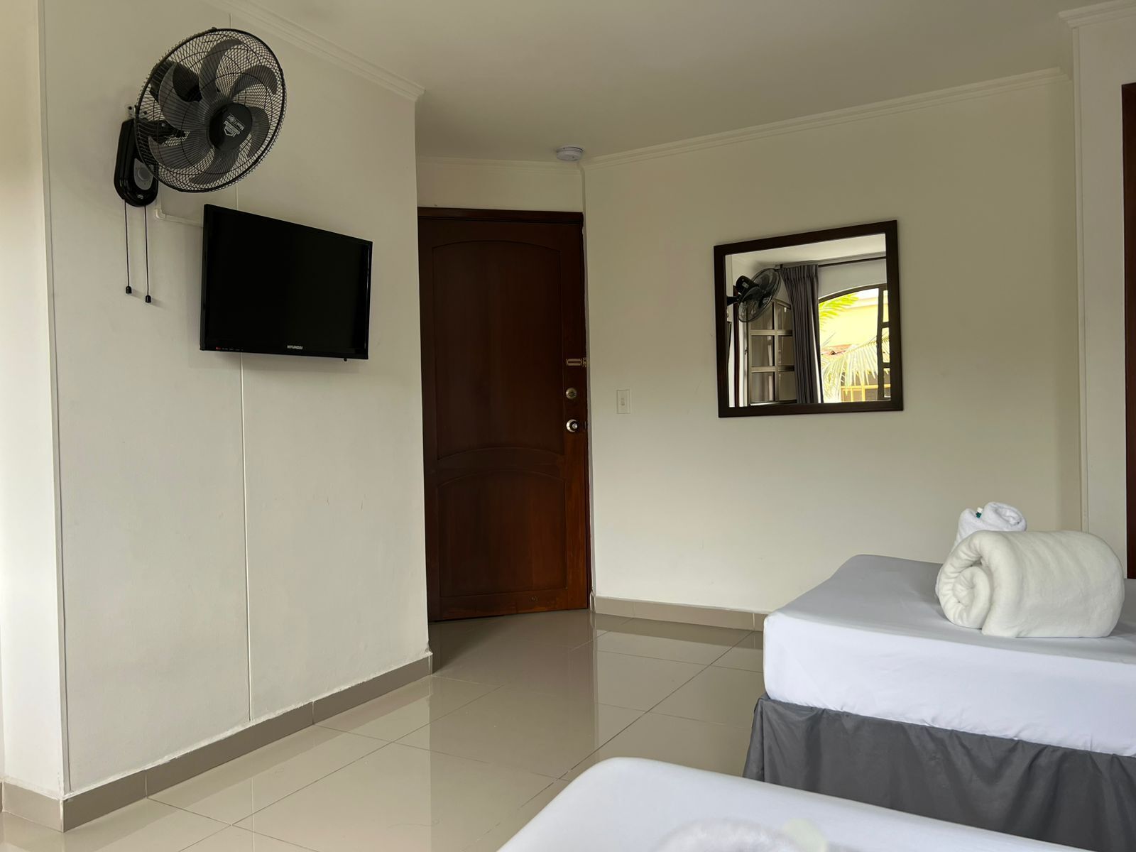 Una habitación de hotel con televisión, ventilador, espejo y cama con toalla.