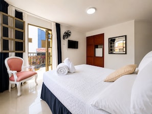 Une chambre d’hôtel avec un lit, une chaise, une télévision, une armoire et un balcon donnant sur des immeubles.