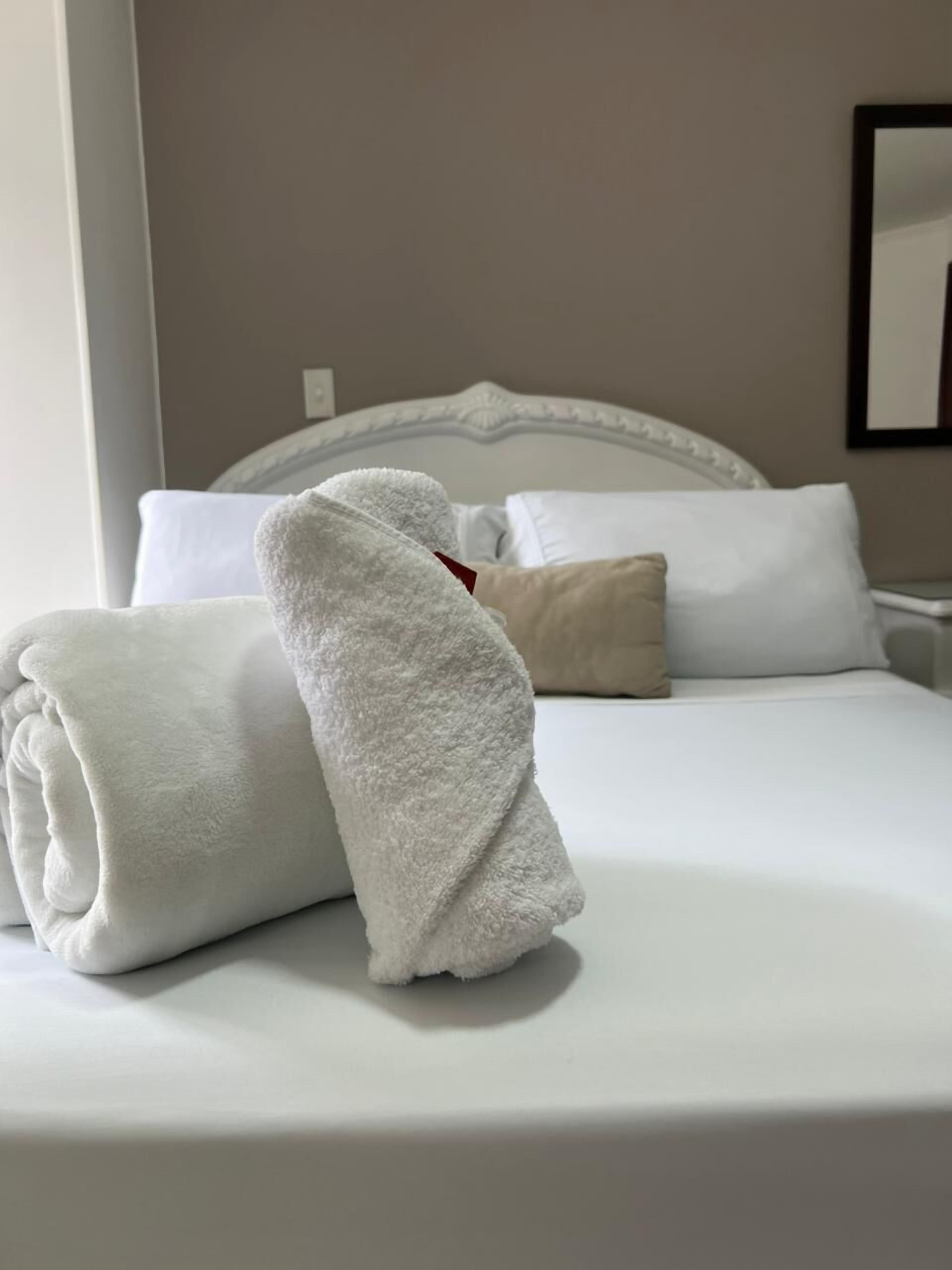A neatly made bed with white linens and a rolled white towel.