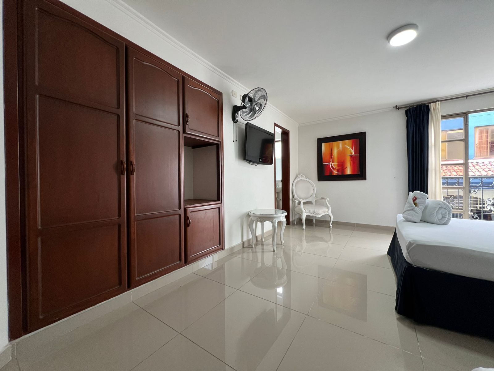 Habitación de hotel con un armario grande, una cama, una mesita, una silla, un televisor y una ventana con vistas.