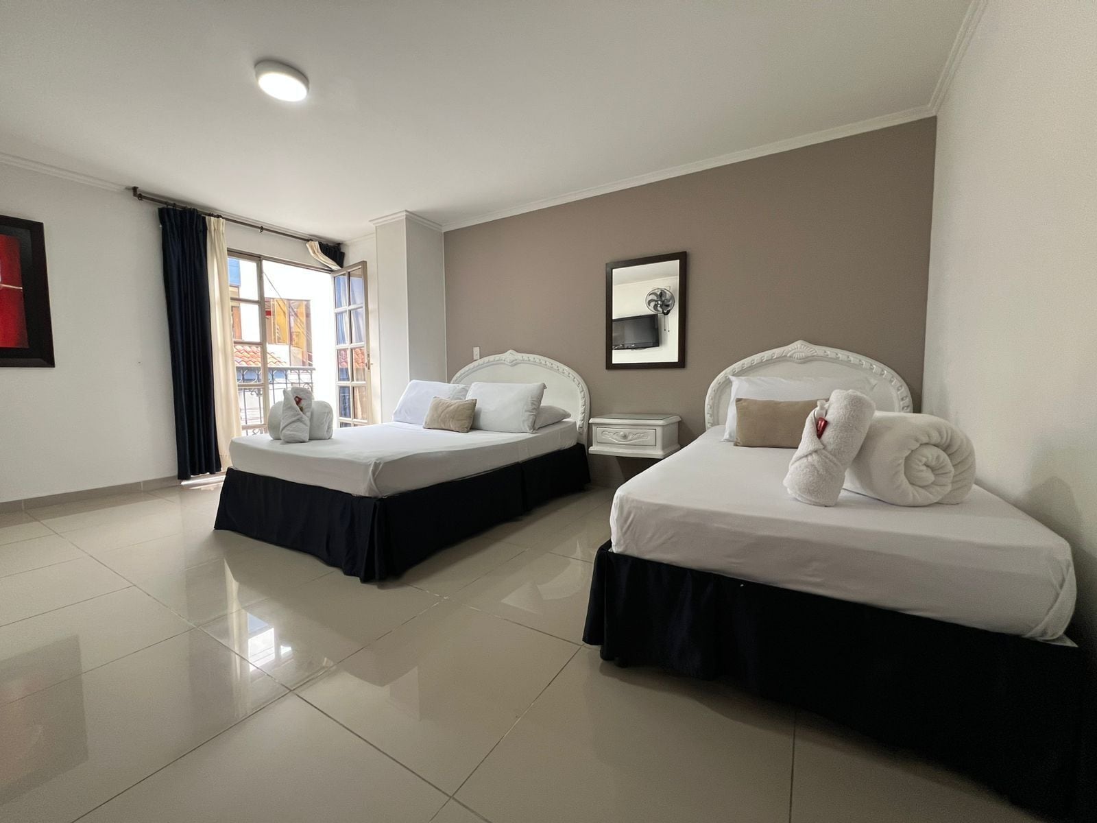Une chambre d’hôtel avec deux lits, un téléviseur à écran plat, un tableau encadré au mur et une fenêtre avec des rideaux.