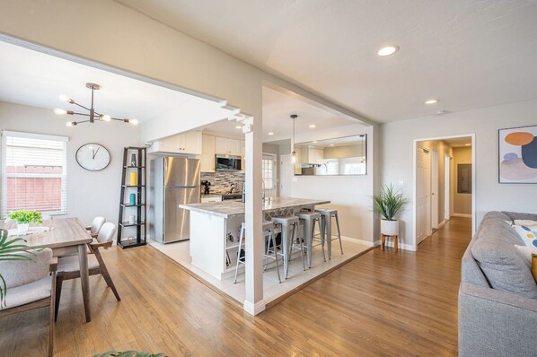 A modern kitchen with a central island, bar stools, and a dining area with a table and chairs.