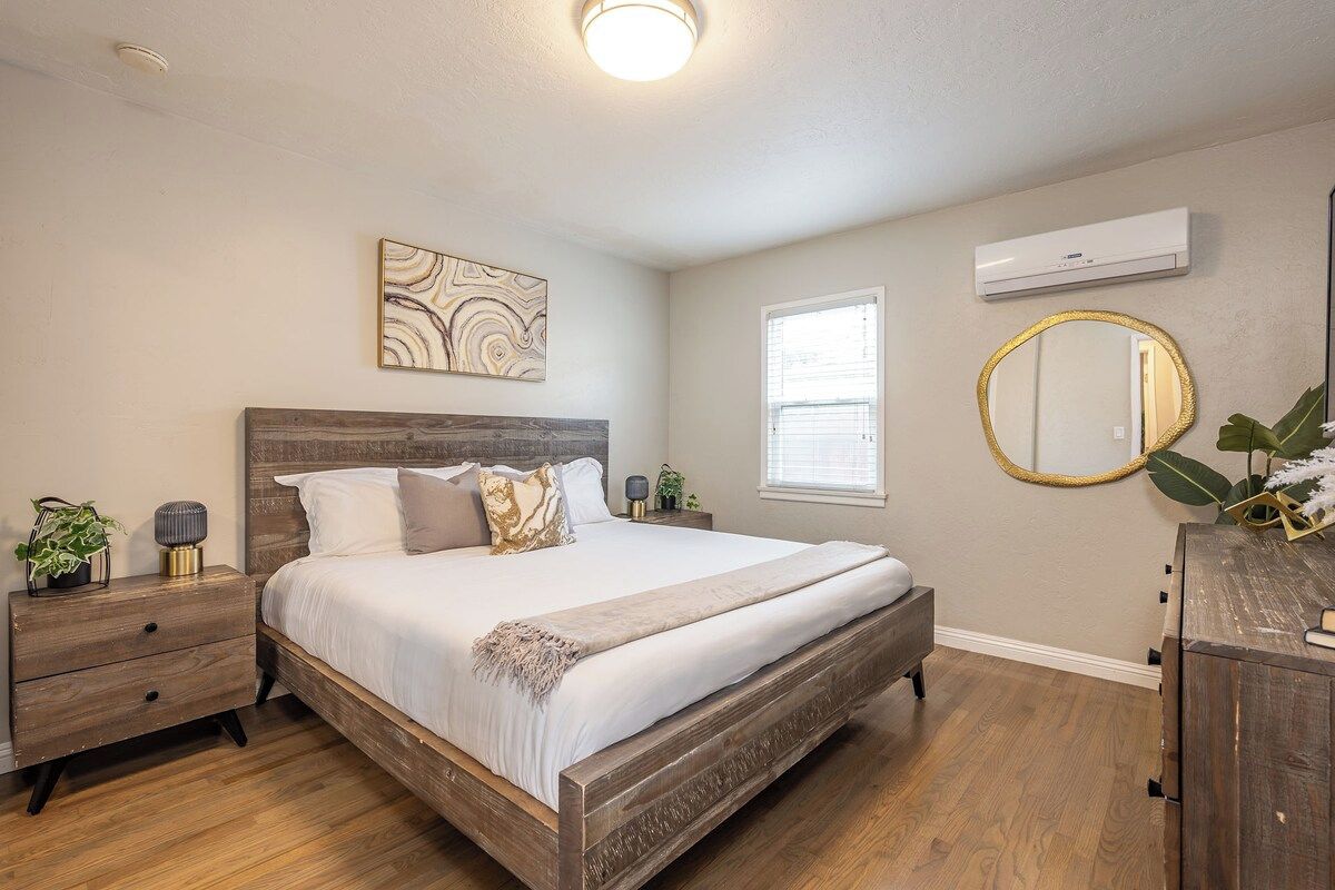 A bedroom with a wooden bed, a nightstand, a wall-mounted mirror, and a window.