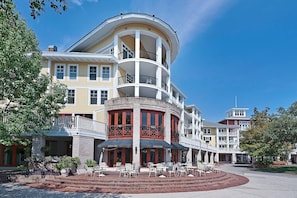 A multi-story hotel with a curved facade, outdoor seating area, and a central courtyard. - Market Street Inn 234 (Miramar Beach)