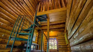 A log cabin interior with a wooden staircase, a window with a view, and a wooden door. - Log Cabin Home  3 Private Acres (Wimberley)