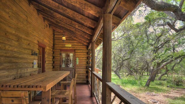 A wooden cabin with a porch, a dining table, and chairs. - Log Cabin Home  3 Private Acres (Wimberley)