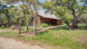 A rustic log cabin with a porch, surrounded by trees and a dirt path. - Log Cabin Home  3 Private Acres (Wimberley)