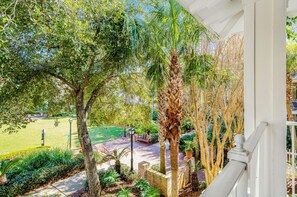 Blick von einem Balkon auf einen Garten mit Palmen, einer Rasenfläche und einem Ziegelweg.