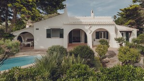 En hvid villa med swimmingpool, omgivet af grønt og træer.
