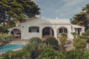 Eine weiße Villa mit Swimmingpool, umgeben von viel Grün und Bäumen.