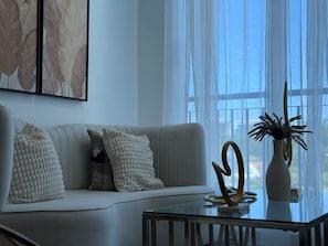 Un salon moderne avec un canapé, des coussins décoratifs, une table basse en verre et un vase avec une plante.