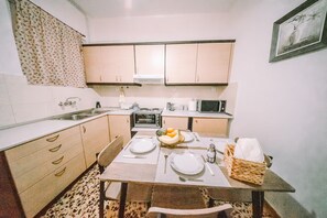Une cuisine compacte comprenant une table à manger pour deux personnes, un four à micro-ondes, un four traditionnel et un évier.