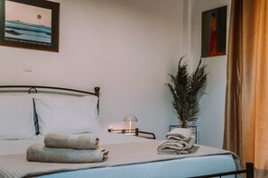 Un lit bien fait, avec des oreillers et des serviettes, une lampe de chevet, un tableau encadré au mur et une plante en pot.