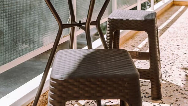 A balcony with a round table and two wicker chairs, a potted plant, and a view of a building with balconies. - 'Stoa Apartment' at Rethymno center (Rethymno)