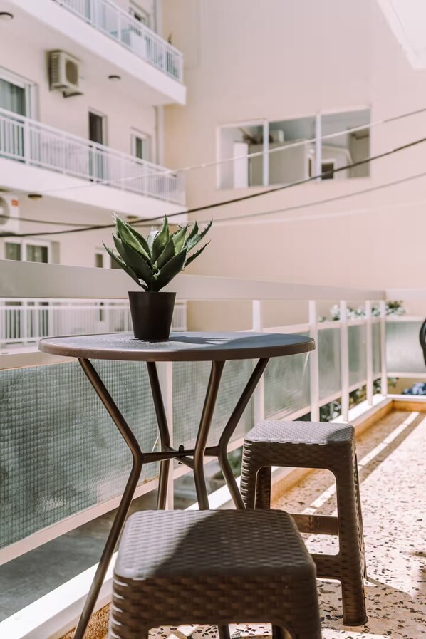 A balcony with a round table and two wicker chairs, a potted plant, and a view of a building with balconies. - 'Stoa Apartment' at Rethymno center (Rethymno)