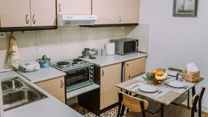 A compact kitchen with a stove, microwave, and a sink. There is a dining table set with plates and a basket of fruit. - 'Stoa Apartment' at Rethymno center (Rethymno)