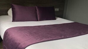 Un lit avec une literie blanche et violette, un plancher en bois et un mur foncé.