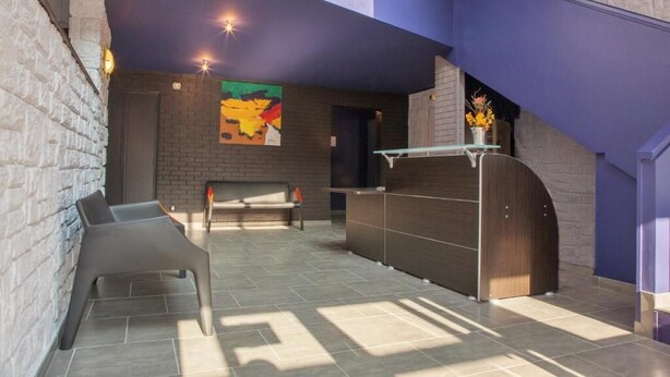 Un hall d’entrée avec un comptoir de réception, un espace salon et une peinture abstraite aux couleurs vives accrochée au mur.