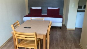 Une pièce de taille modeste comprenant un lit, une petite kitchenette et un coin repas avec une table et des chaises.