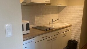 Une cuisine de taille réduite avec des meubles blancs, un plan de travail en bois, un évier, un four à micro-ondes et une poubelle.