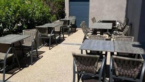 Une terrasse extérieure avec des tables et des chaises, une porte de garage bleue et de la verdure en arrière-plan.