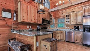 A wooden cabin-style kitchen with a granite countertop, wooden cabinets, a stainless steel refrigerator, and a built-in bench. - Blue Ridge Overlook Lodge | Blue Ridge, GA (Cherry Log)