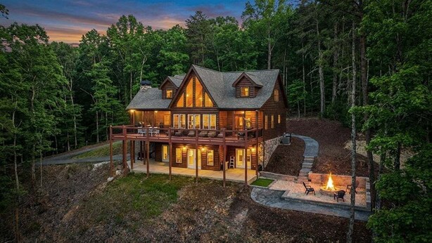 A large log cabin with a deck, surrounded by dense forest. - Blue Ridge Overlook Lodge | Blue Ridge, GA (Cherry Log)