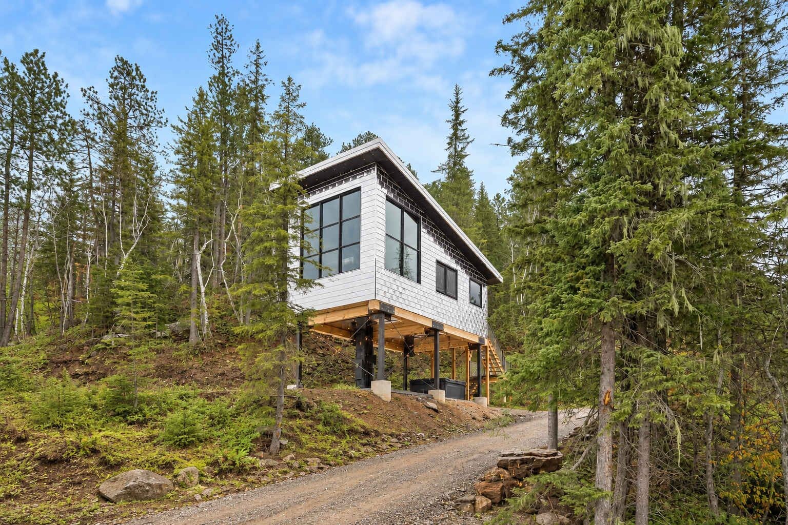 A modern two-story cabin with a large window on the upper floor, surrounded by a forest.