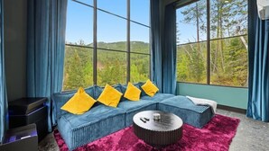 A room with a large window, a blue sofa with yellow pillows, a round coffee table, and a red rug.