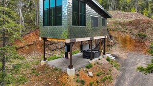 A modern cabin with a glass facade, elevated on stilts, surrounded by forest.