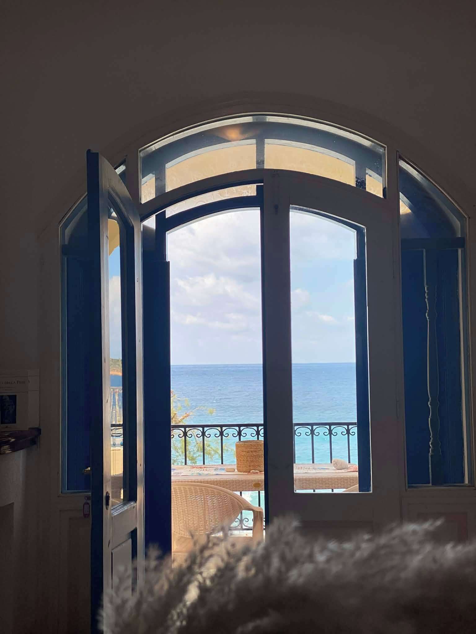 An open door leading to a balcony with a view of the sea.