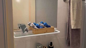 Un bagno con lavandino bianco, uno specchio, un portasciugamani e uno scaffale con articoli da toilette.