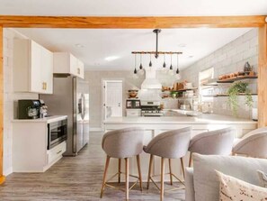 Une cuisine moderne avec des meubles blancs, des appareils en acier inoxydable et un îlot central doté de tabourets de bar.