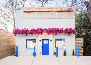 A two-story building with a blue door and windows, surrounded by a white fence and pink flowers. - 50% Off! End Summer Right! Pool + Sauna + Hot Tub (Charlotte)