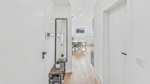 Un couloir moderne avec un plancher en bois, des murs blancs et un coin repas à l’arrière-plan.