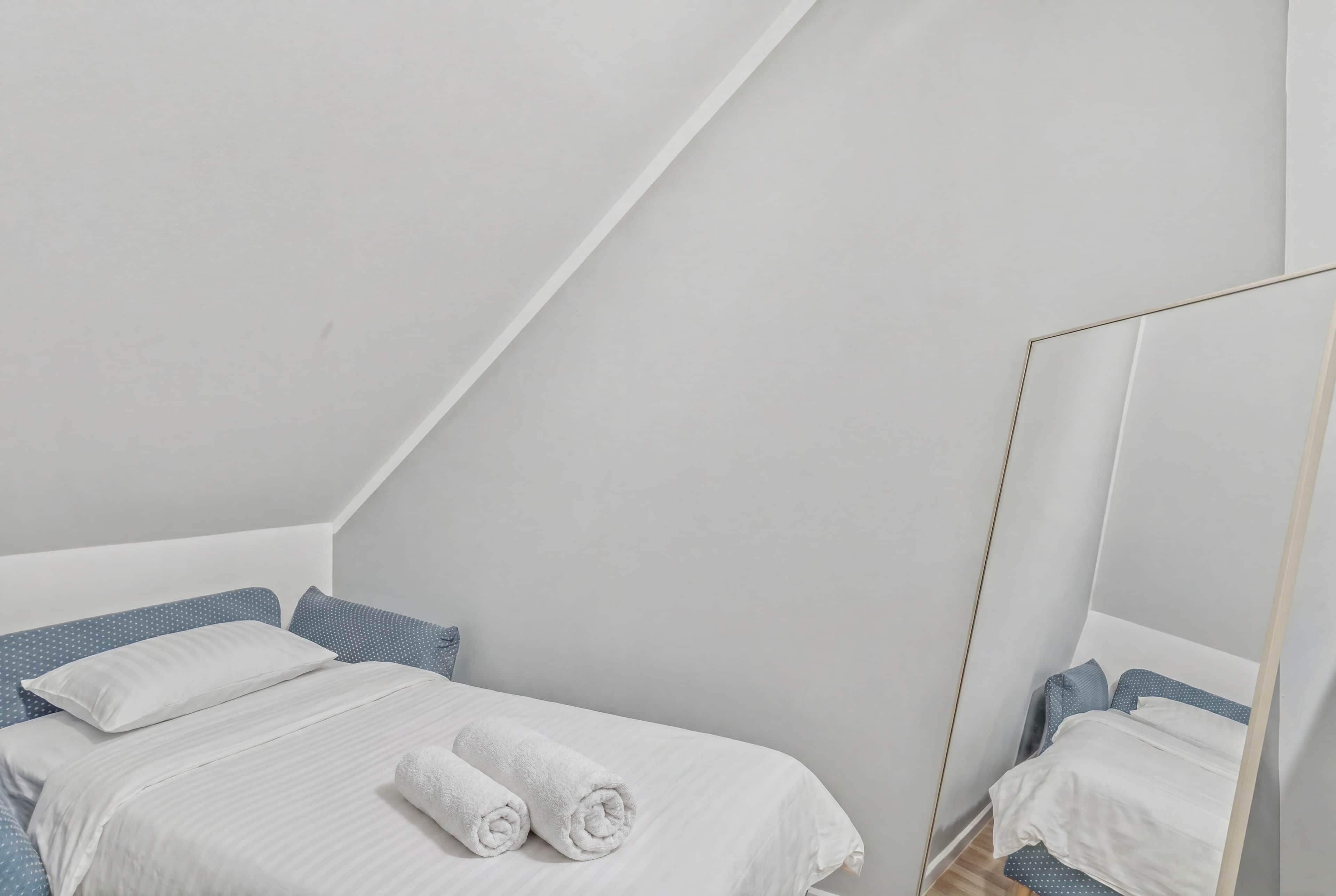 A bedroom with a bed, pillows, a rolled towel, and a mirror.