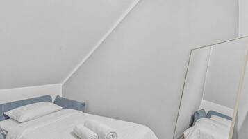 A bedroom with a bed, pillows, a rolled towel, and a mirror.