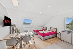 Een moderne loftkamer met een eethoek, twee bedden, een keuken en een aan de muur bevestigde televisie.