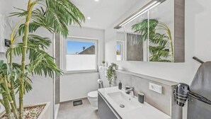 Une salle de bain moderne avec un grand miroir, un lavabo blanc, des toilettes et une plante en pot.