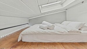 A bedroom with a sloped ceiling, a bed with white bedding, and a skylight.