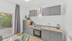 A modern kitchen with grey cabinets, a stainless steel sink, a built-in oven, and a window overlooking greenery.