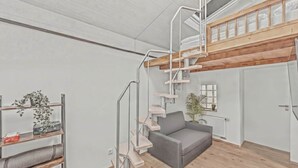 A modern interior with a wooden loft, a grey sofa, and a staircase with a metal railing.