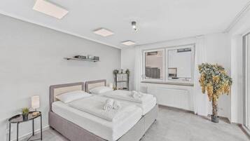 Ein modernes Schlafzimmer mit Doppelbett, Nachttischen, Heizkörper, einem fenster mit Vorhängen und einer Topfpflanze.